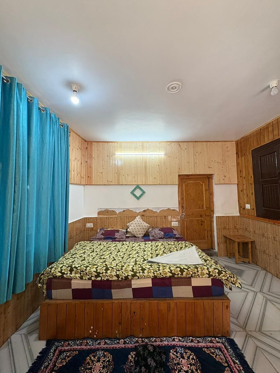 A bedroom with a bed, curtains, a wooden door, and a small table.