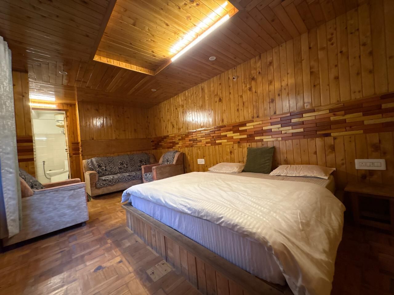 A wooden-paneled room with a bed, two armchairs, a small table, and a built-in bench.