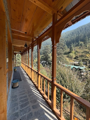 A wooden balcony with stone flooring, overlooking a forested valley.