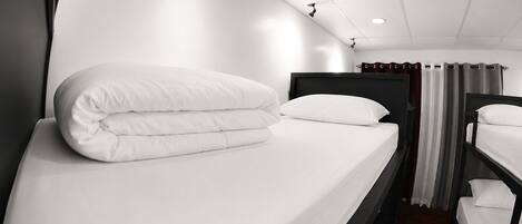 Habitación de hotel con una cama individual, cabecera, mesita de noche, espejo y ventana con cortinas.