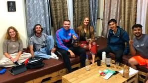 A group of people seated on benches and sofas in a room with wooden flooring and a wooden coffee table. - Jungle Nairobi Backpackers Hostel (Nairobi)