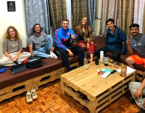 A group of people seated on benches and sofas in a room with wooden flooring and a wooden coffee table. - Jungle Nairobi Backpackers Hostel (Nairobi)