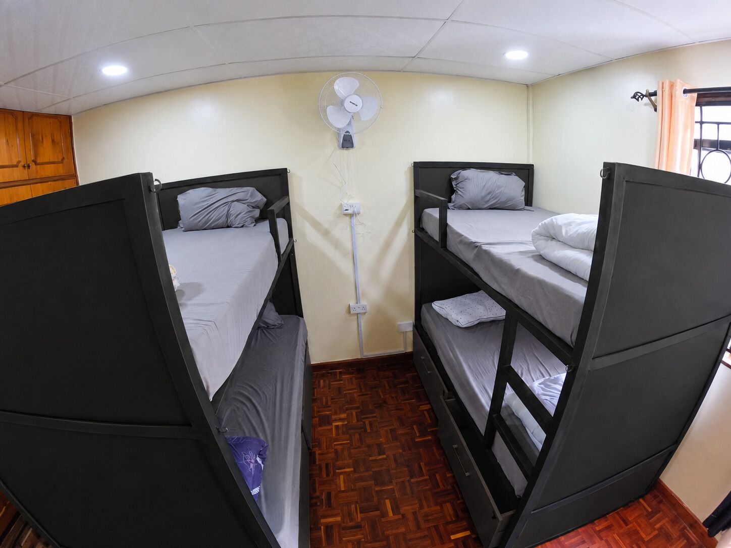A room with bunk beds, a wall-mounted fan, and a window with curtains.