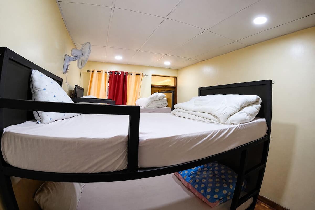 A bunk bed with white bedding, a ceiling fan, and a window with curtains.