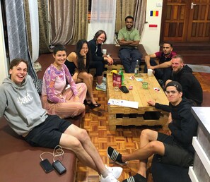 A group of people seated around a wooden table in a room with a herringbone floor pattern. - Jungle Nairobi Backpackers Hostel (Nairobi)