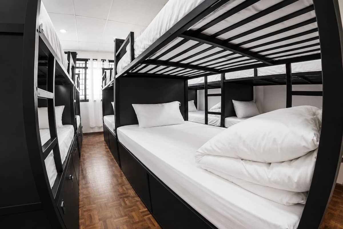 A bunk bed room with a wooden floor, black metal frame, and white bedding.