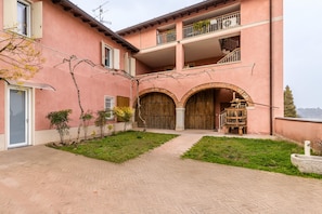 Ein rosafarbenes Gebäude mit einem zentralen Innenhof, einer Holztür und einem Balkon mit Pflanzen.