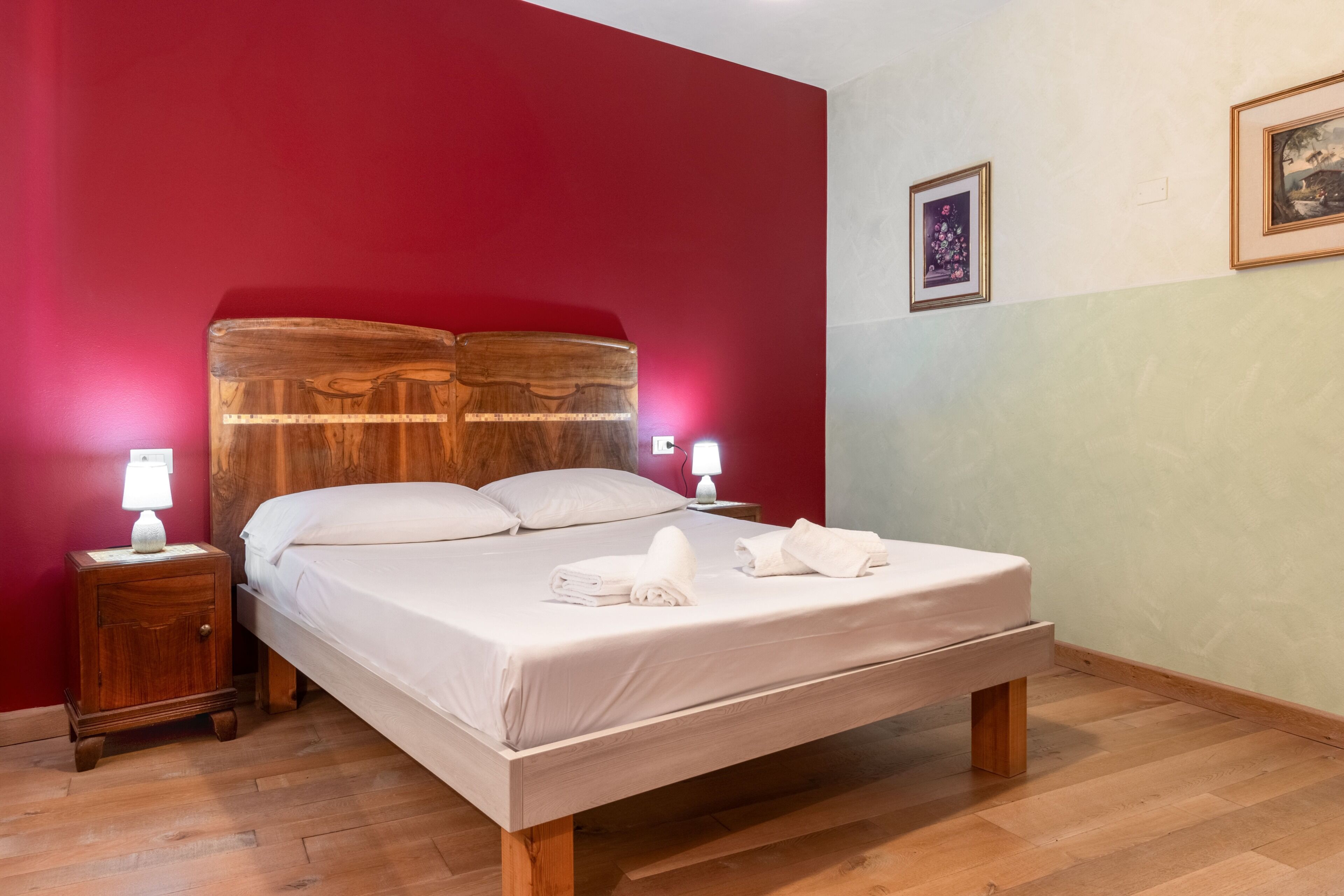 A bedroom with a wooden bed, white linens, a nightstand with a lamp, and a framed picture on the wall.