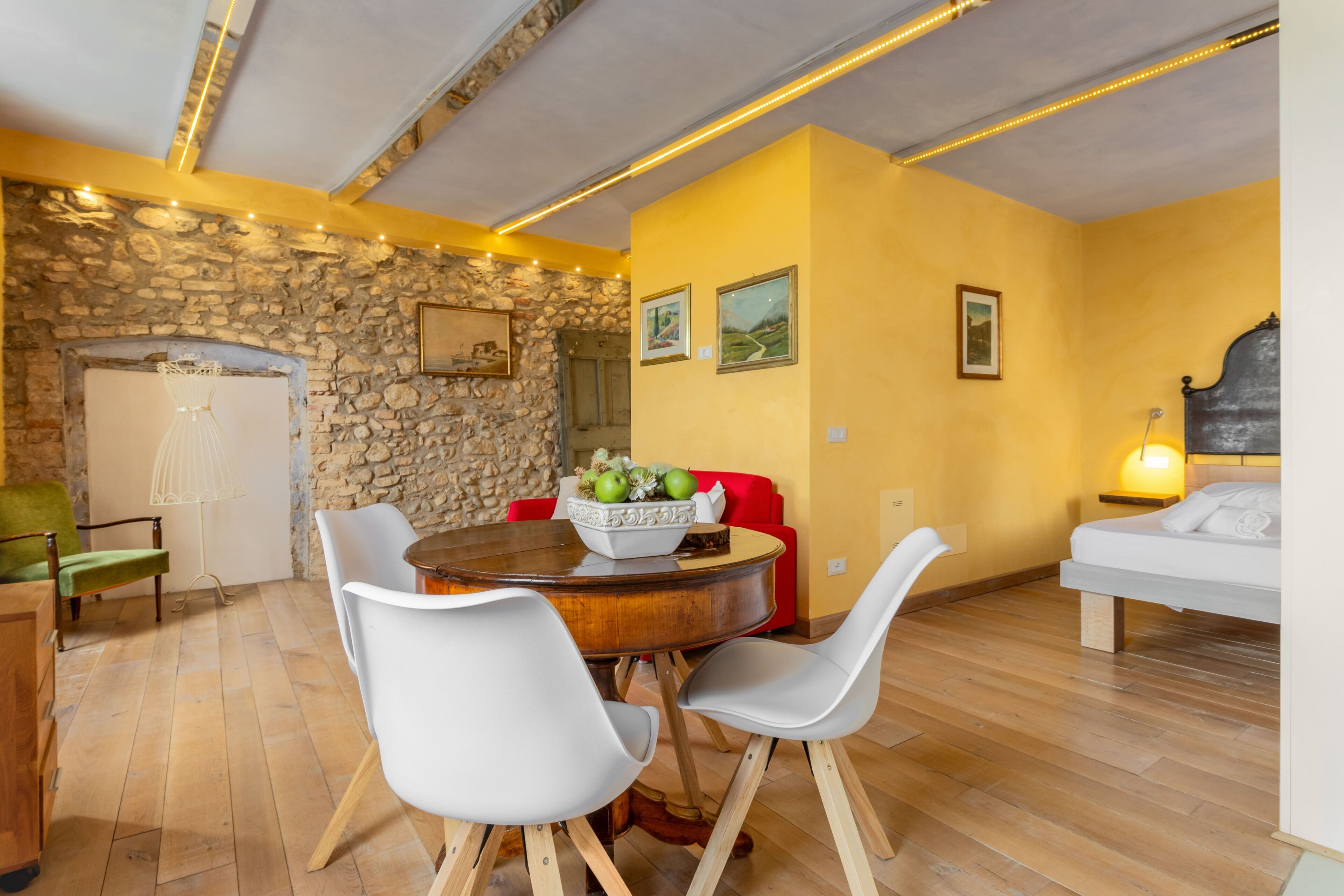 Uma sala de jantar com parede de pedra, mesa de madeira redonda e cadeiras brancas.