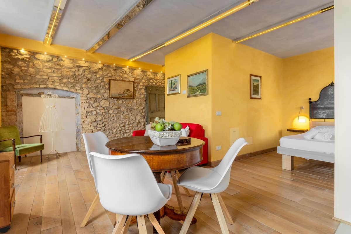 Uma sala de jantar com parede de pedra, mesa de madeira redonda e cadeiras brancas.
