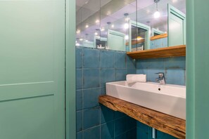 Ein Badezimmer mit Waschbecken, blauen Fliesen, einer Holzablage und einem Spiegel.