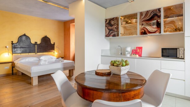 A modern hotel room with a bed, bedside table, round wooden table, white chairs, and a kitchen area with a microwave. - Borgo al Sole by Wonderful Italy (Castello)