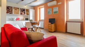 A modern living room with a red sofa, a dining area with a table and chairs, a television, and artwork on the walls. - Borgo al Sole by Wonderful Italy (Castello)