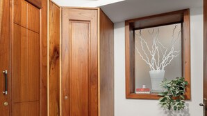 A corner room with wooden cabinets, a bench, a window with a plant, and a wall-mounted mirror.
