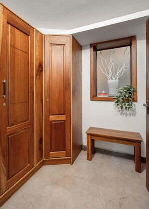 A corner room with wooden cabinets, a bench, a window with a plant, and a wall-mounted mirror.