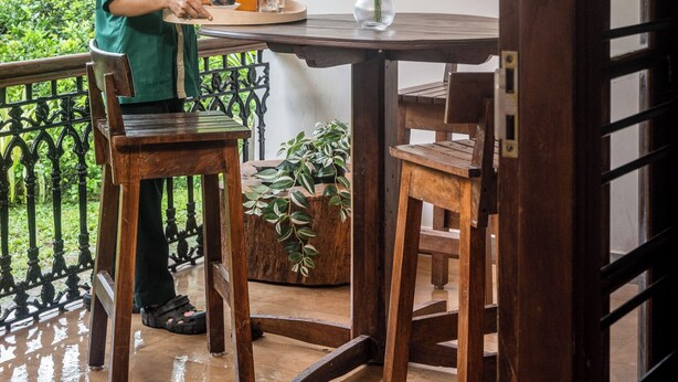 A person at a wooden table with a glass of orange juice, a vase with flowers, and a potted plant.
