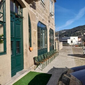 A stone building with green doors and windows, outdoor seating, and a cobblestone path.