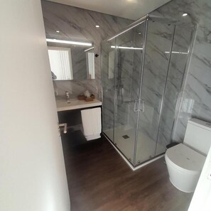 A modern bathroom with a glass shower enclosure, a marble-tiled wall, and a white toilet. - DOURO B&B Avenida (CALDAS DE ARÊGOS)