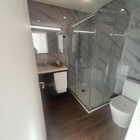 Un baño moderno con mampara de vidrio, pared con azulejos de mármol y un inodoro blanco.