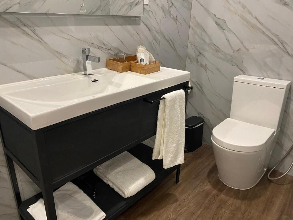 Une salle de bain avec un lavabo blanc, un meuble-lavabo noir, des toilettes blanches et des murs en marbre.