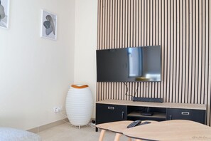 Ein modernes Wohnzimmer mit einem flachbildfernseher an einer Holzwand, einer weißen Dekovase und einem kleinen Tisch mit Fernbedienung.