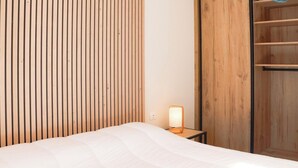 A hotel room with a bed, a bedside table with a lamp, a wooden wardrobe, and a shelf with folded towels. - Magnificent sea view from this apartment (Agde)