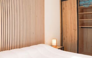 Ein Hotelzimmer mit einem Bett, einem Nachttisch mit Lampe, einem Holzschrank und einem Regal mit gefalteten Handtüchern.