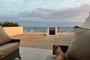 Blick auf einen Strand mit einem Zaun, einem Tor und einer Person, die auf einem Stuhl sitzt.