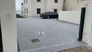 A modern building with a car parked in front, a compass-like design on the ground, and a view of the sea. - Magnificent sea view from this apartment (Agde)