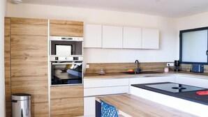 A modern kitchen with built-in appliances, white cabinetry, and a wooden accent wall. - Magnificent sea view from this apartment (Agde)
