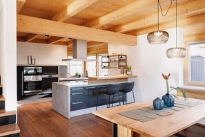 Eine moderne Küche mit Holzbalken, einer zentralen Kochinsel, Barhocker und Pendelleuchten.