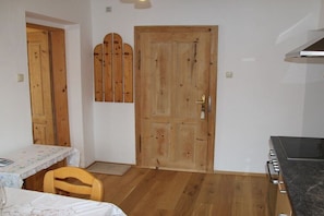 Eine Küche mit Holzboden, einem Herd, einem Tisch mit Stuhl und einer Tür mit Holzpaneelen.