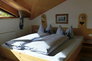 Ein hölzernes Bett mit karierter Bettwäsche, ein Fenster mit Vorhängen und ein gerahmtes Bild an der Wand.