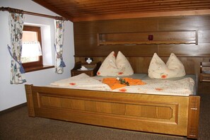 A wooden bed with a floral bedspread, a nightstand with a decorative item, and a window with curtains. - Holiday apartment with 2 bedrooms (Krimml)
