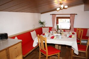 A dining area with a table set for four, red upholstered chairs, a wooden bench, and a radio on a counter. - Holiday apartment with 2 bedrooms (Krimml)