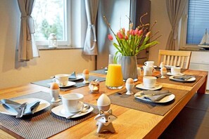 Ein Frühstückstisch ist gedeckt mit Tellern, Tassen und einer Blumenvase.