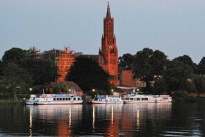 Ein Fluss mit drei angedockten Booten, einem markanten Kirchturm und umliegenden Gebäuden.