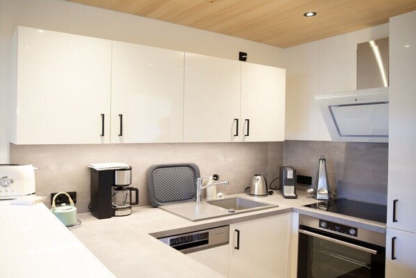 A modern kitchen with white cabinets, a stainless steel range hood, a built-in dishwasher, and a coffee maker. - Apartment in Mittelberg with swimming pool (Mittelberg)