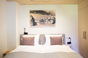 A bedroom with a bed, a nightstand, a wall-mounted lamp, and a picture of people in a field. - Apartment in Mittelberg with swimming pool (Mittelberg)