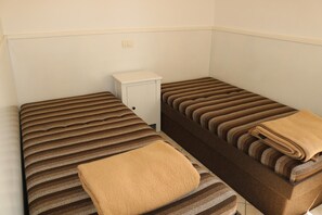 Zwei Einzelbetten mit gestreifter Bettwäsche, ein kleiner weißer Nachttisch und eine beige Decke auf einem Bett.