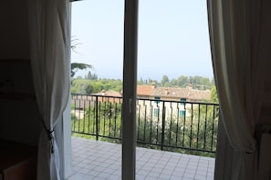 Ein Balkon mit Blick auf eine Wohngegend, ein Fliesenboden und teilweise gezogene Vorhänge.