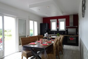 Ein Essbereich mit einem Tisch für vier Personen, Korbstühle, einer schwarzen Tischdecke und einer Küche im Hintergrund.