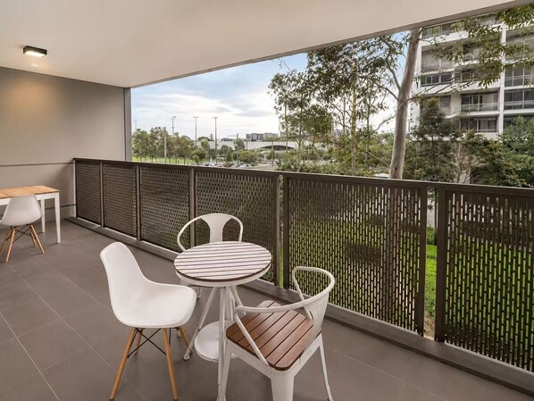 A balcony with a table and chairs, a view of the cityscape, and a modern building in the background.