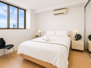 A hotel room with a large bed, two bedside tables, a chair, a window, and an air conditioning unit.