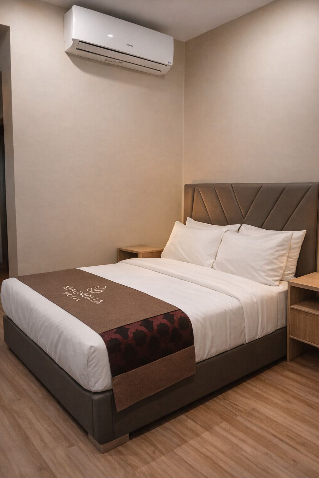 Ein Hotelzimmer mit Bett, Nachttisch, Holzboden und Klimaanlage.