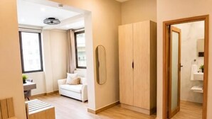 A modern hotel room with a wooden floor, a white sofa, a wooden wardrobe, and a mirror.