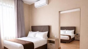 A hotel room with a bed, bedside table, nightstand, and an air conditioning unit.