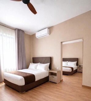A hotel room with a bed, bedside table, nightstand, and an air conditioning unit. - Magnolia Suites B&B (Dar es Salaam)
