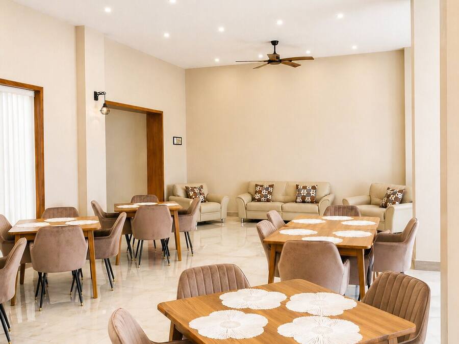 A spacious dining area with multiple tables and chairs, a ceiling fan, recessed lighting, and a large window.
