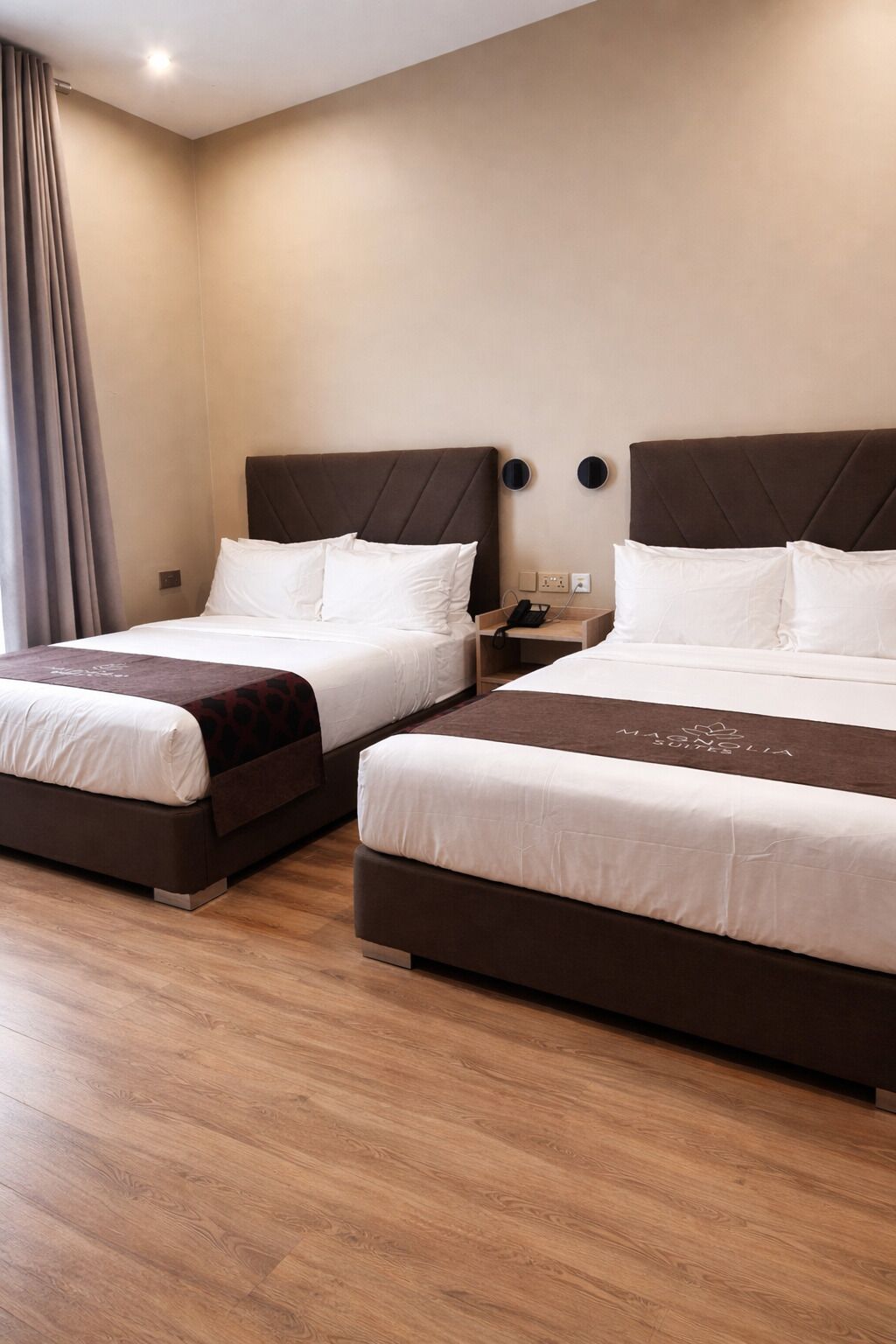 A hotel room with two beds, a wooden floor, and a nightstand with a phone.